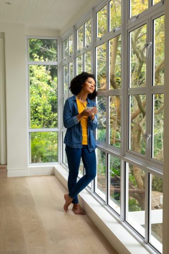 Biracial woman holding cup of coffee and looking out window at home. Relaxation, lifestyle and domestic life, unaltered.